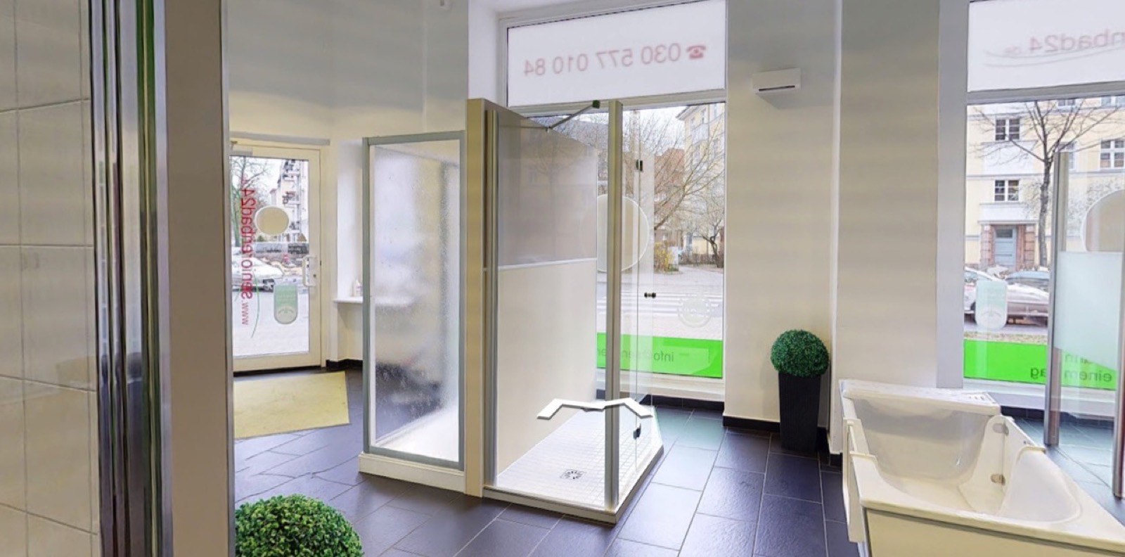 Blick in die Ausstellung: eine bodenebene Dusche in der Mitte, rechts eine Sitzbadewanne, dahinter die Schaufensterfront zur Straße
